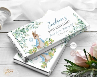 May include: Printable chocolate bar wrapper featuring a watercolor illustration of Peter Rabbit with a blue balloon, surrounded by green leaves. The wrapper is white with blue text that reads "Jackson's 2nd Birthday Thank You for Hopping by! 5.18.2045".