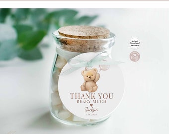 May include: A round, white thank you tag with a brown teddy bear wearing a party hat and holding a pink balloon. The tag says "Thank You Beary Much" with a heart and the name "Jackson" and the date "5.18.2028".