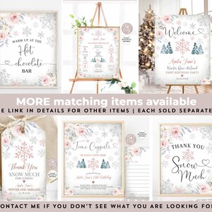 May include: Printable winter wonderland party signs with pink and blue snowflakes, trees, and floral accents. The signs include a welcome sign, a hot chocolate bar sign, a thank you sign, and a time capsule sign. The signs are perfect for a first birthday party.