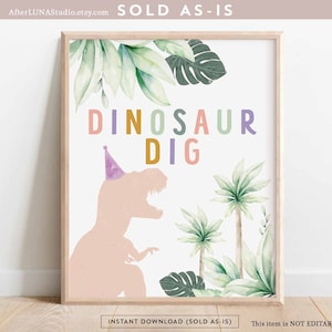 May include: A framed print with a light wood frame. The print features the words "DINOSAUR DIG" in colorful letters, a pink dinosaur silhouette wearing a party hat, and watercolor-style tropical leaves. The text "INSTANT DOWNLOAD (SOLD AS-IS)" is at the bottom.