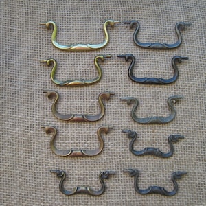 May include: Ten antique brass drawer pulls with a decorative, curved design. The pulls are arranged in rows of two, with the top row being the largest and the bottom row being the smallest.