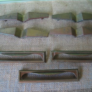 May include: Set of eight vintage brass drawer pulls in various styles. Some are curved, some are straight, and some have a more modern design. All are in good condition with a warm, aged patina.