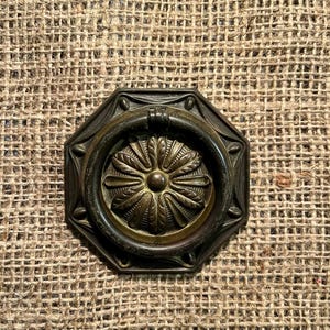 May include: Antique bronze drawer pull with a floral center and a ring handle. The octagonal base features decorative detailing. The hardware has a vintage aesthetic.