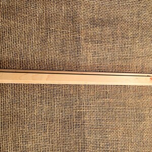 May include: A light-colored wooden picture frame with a dark stripe along the top edge. The frame is rectangular and has a small hole on one end. The background is a rough, woven fabric.