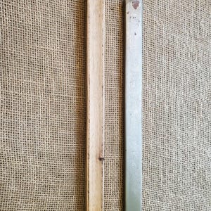 May include: Two rectangular pieces of wood and metal are displayed vertically against a burlap background. One is a light-colored wood, and the other is a muted green metal. Both pieces are long and narrow, with the wood piece showing a natural grain.