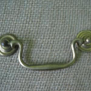 May include: A silver metal drawer pull with a rounded, decorative design. The pull has a simple, curved shape and is ideal for adding a touch of vintage style to furniture.