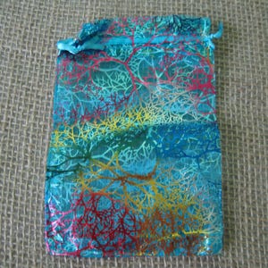 May include: A turquoise blue organza gift bag with a colorful, abstract, floral pattern. The bag has a drawstring closure.