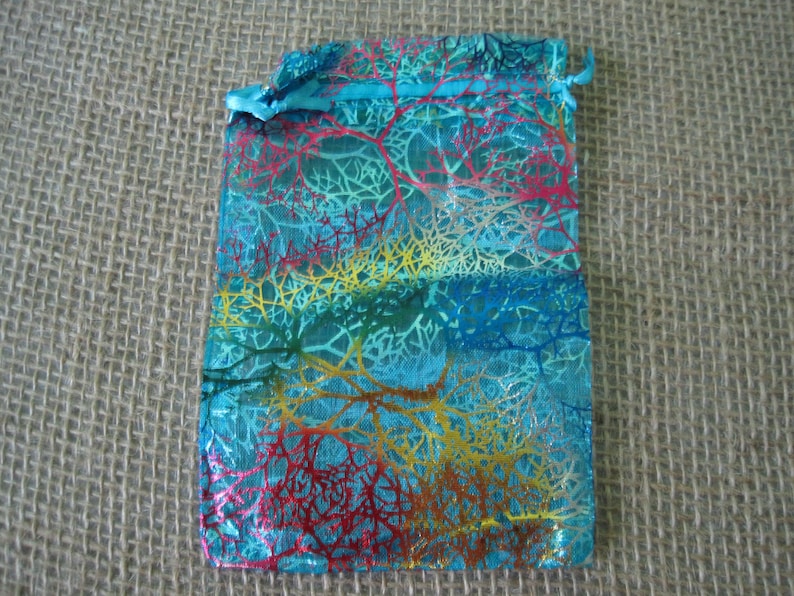 May include: A turquoise blue organza gift bag with a colorful, abstract, floral pattern. The bag has a drawstring closure.