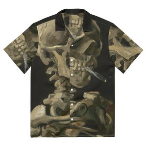 Puede incluir: Una camisa de manga corta con botones, fondo negro y un patrón repetido de una pintura de una calavera sosteniendo un cigarrillo. La calavera está pintada en tonos de marrón, amarillo y verde.