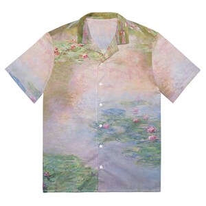 Puede incluir: Una camisa de manga corta con botones y un estampado abstracto colorido de nenúfares sobre un fondo azul claro. La camisa tiene cuello y un corte holgado.