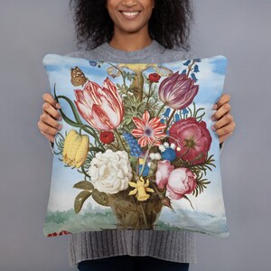 May include: A blue and white throw pillow with a vintage floral print featuring a bouquet of red, pink, yellow, and blue flowers with a butterfly. The flowers are arranged in a vase with a brown and white pattern.