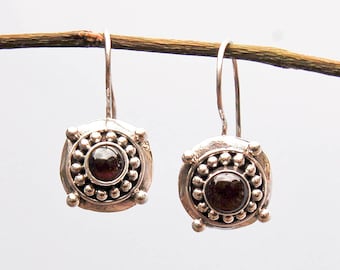 May include: A pair of silver earrings with a dark red gemstone set in a circular design with a beaded border.