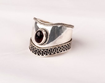 May include: A silver ring with a dark brown gemstone set in a silver bezel. The ring has a wide band with a decorative border.