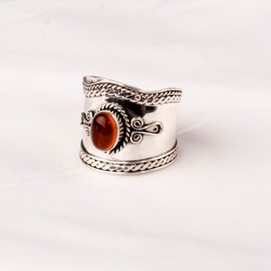 May include: A silver ring with an orange gemstone set in a decorative silver bezel. The ring has a wide band with intricate silver designs.