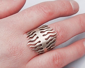 May include: A silver ring with a flame design. The ring is made of metal and has a cutout design.