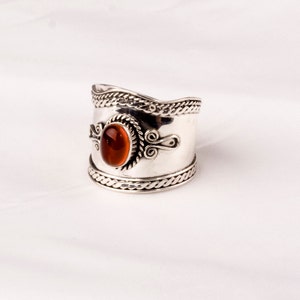 May include: A silver ring with an orange gemstone set in a decorative silver bezel. The ring has a wide band with intricate silver designs.