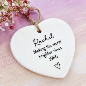Handmade personalised ceramic heart ornament for women, custom birthday keepsake gift reading “Making the world brighter since 1986”, minimalist heart decoration.