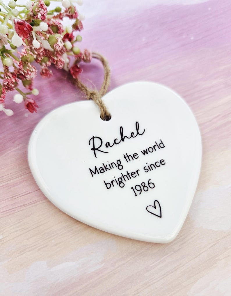 Handmade personalised ceramic heart ornament for women, custom birthday keepsake gift reading “Making the world brighter since 1986”, minimalist heart decoration.