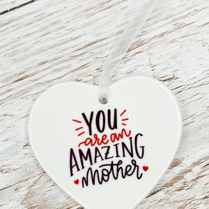 May include: White ceramic heart-shaped ornament with the text "YOU are an AMAZING mother" in black and red lettering.