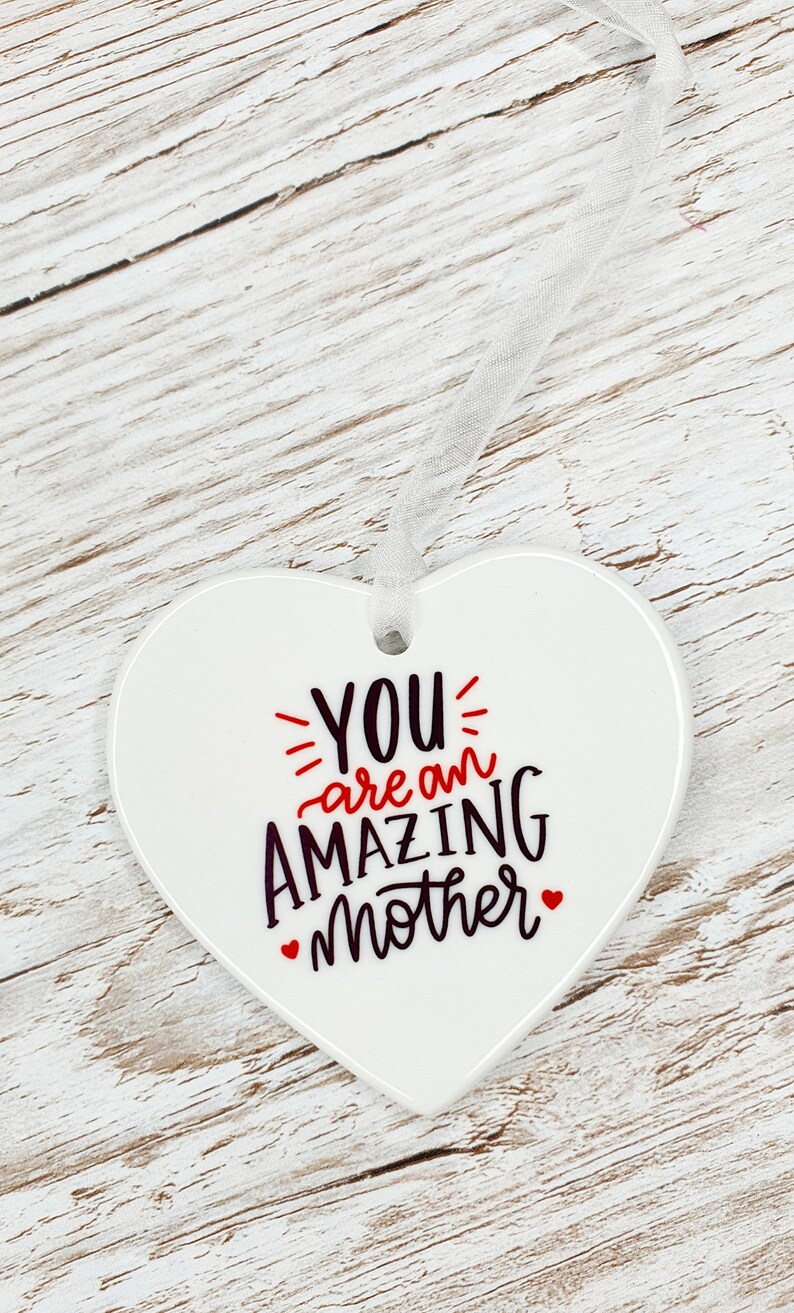 May include: White ceramic heart-shaped ornament with the text "YOU are an AMAZING mother" in black and red lettering.