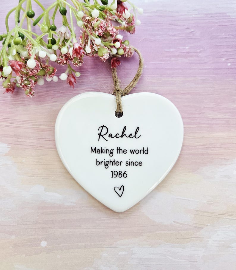 Personalised ceramic heart keepsake gift with custom name and birth year, handmade birthday decoration for her, white ceramic hanging heart ornament with floral styling.