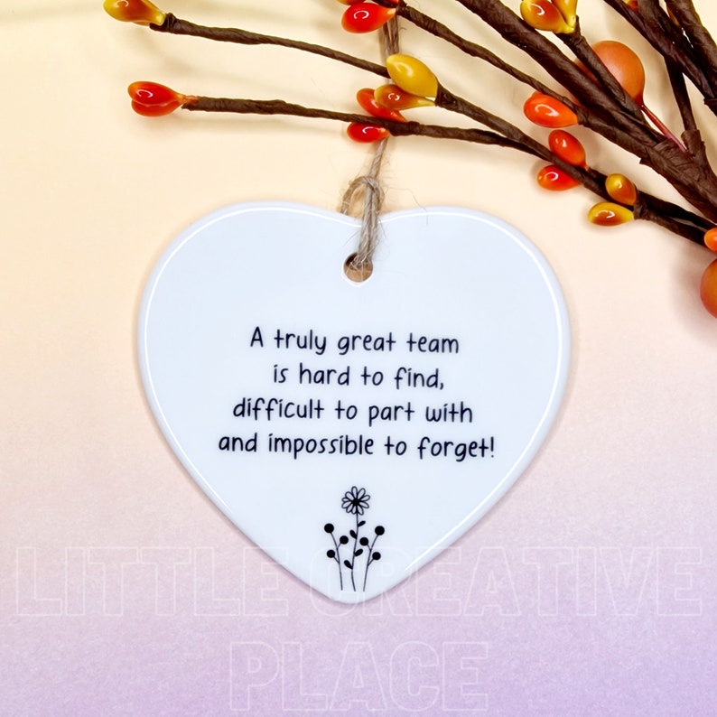 May include: White heart-shaped ceramic ornament with a jute string for hanging. The ornament has the text "A truly great team is hard to find, difficult to part with and impossible to forget!" and a small floral design.