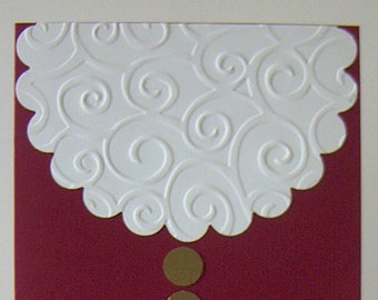 May include: A red card with a white scalloped edge with a swirl pattern. The card has a black belt with a gold buckle and two gold circles.