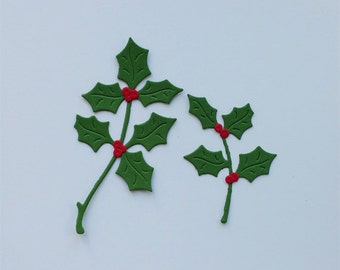 May include: Two flat, die-cut holly sprigs made of green material with pointed, serrated leaves and small clusters of bright red berries. The larger sprig features three leaf sections, while the smaller sprig has two leaf sections.