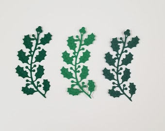 May include: Three dark green holly leaf sprigs with detailed leaf and berry cutouts are arranged on a white background. The sprigs vary slightly in shade, creating a subtle visual contrast. Ideal for holiday crafts.