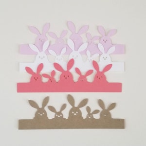 May include: A collection of paper bunny cutouts in various colors, including pink, white, red, and brown. Each cutout features a row of bunny silhouettes, perfect for Easter or spring-themed crafts and decorations.