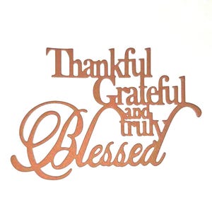 May include: A copper-colored metal sign with the words "Thankful, Grateful, and Truly Blessed" in a decorative font. The sign is cut out and has a warm, inviting appearance, perfect for home decor.
