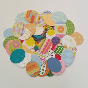 May include: A collection of colorful paper circles with various patterns, including polka dots, stripes, and floral designs. The circles are arranged in a circular pattern, resembling a bouquet of flowers.