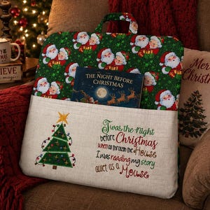 May include: A rectangular fabric book pillow with a handle, featuring a green top section with a repeating Santa Claus pattern and a beige bottom pocket. The pocket displays an embroidered Christmas tree and the text 'Twas the night before Christmas when all through the house I was reading my story quiet as a mouse'.