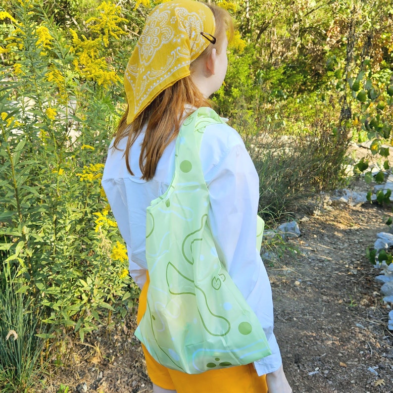 May include: A person wearing a yellow bandana with a white pattern and a white shirt is carrying a light green reusable shopping bag with a white pattern.