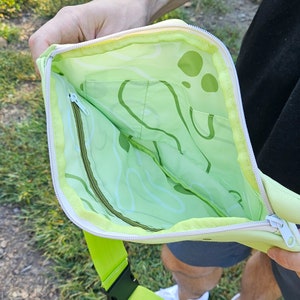 May include: A green and white crossbody bag with a zipper closure and a green and white patterned lining. The bag has a lime green adjustable strap.