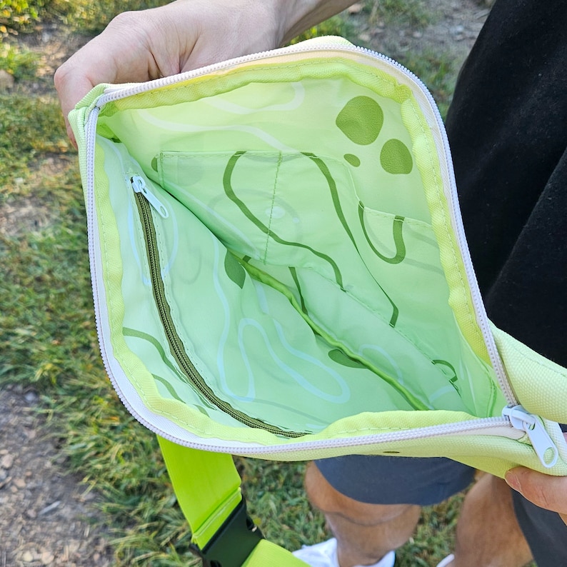 May include: A green and white crossbody bag with a zipper closure and a green and white patterned lining. The bag has a lime green adjustable strap.
