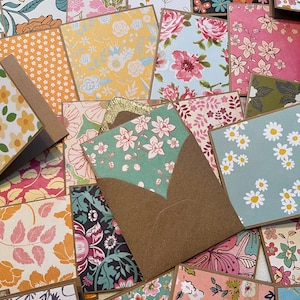 May include: A collection of colorful patterned paper cards with a brown envelope. The cards feature floral and geometric designs in shades of pink, blue, yellow, green, and white.