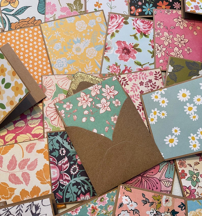 May include: A collection of colorful patterned paper cards with a brown envelope. The cards feature floral and geometric designs in shades of pink, blue, yellow, green, and white.
