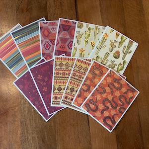 May include: A collection of patterned cards with various designs, including stripes, geometric shapes, cacti, and snakes. The cards feature a white border and are arranged on a wooden surface. The color palette includes red, orange, green, and brown.