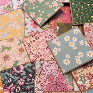May include: A collection of square greeting cards featuring various floral patterns in colors including pink, green, yellow, blue, and dark brown. Each card has a brown paper border and displays distinct botanical illustrations of flowers.
