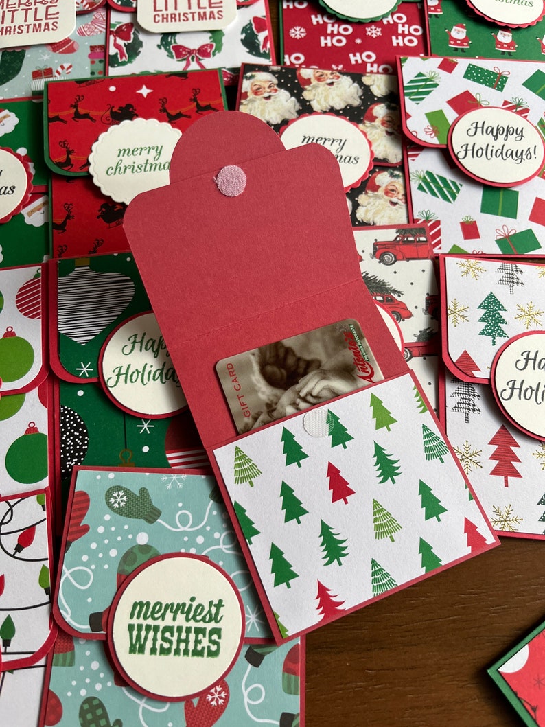 May include: A red and white Christmas gift card holder with a variety of festive patterns. The holder is open and a gift card is visible inside. The holder has a red button closure and the words "merriest wishes" are printed on the front.