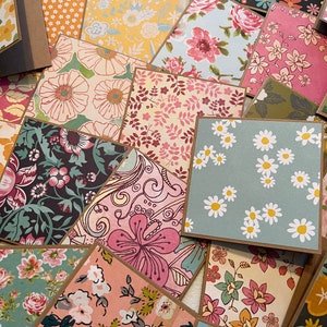 May include: A collection of patterned paper cards with brown borders. The cards feature various floral designs in shades of pink, blue, green, and yellow.