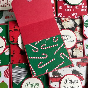 May include: A collection of handmade Christmas cards with various designs. The cards feature red, green, and white colors with festive patterns like candy canes, Santa Claus, and Christmas trees. The cards have the text "merry christmas", "happy holidays", and "yourself a merry little christmas".