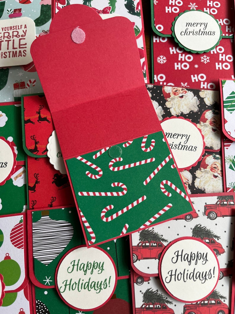 May include: A collection of handmade Christmas cards with various designs. The cards feature red, green, and white colors with festive patterns like candy canes, Santa Claus, and Christmas trees. The cards have the text "merry christmas", "happy holidays", and "yourself a merry little christmas".