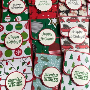May include: A collection of ten handmade Christmas card envelopes with various holiday designs and greetings. The envelopes feature red, green, white, and blue colors with patterns of ornaments, reindeer, Santa Claus, mittens, and Christmas trees. The envelopes have a flap that folds over to create a pocket for cash or a gift card. The envelopes are decorated with festive greetings such as "Merry Christmas", "Happy Holidays", and "Merriest Wishes".