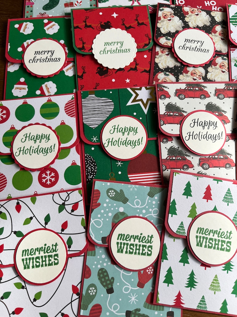 May include: A collection of ten handmade Christmas card envelopes with various holiday designs and greetings. The envelopes feature red, green, white, and blue colors with patterns of ornaments, reindeer, Santa Claus, mittens, and Christmas trees. The envelopes have a flap that folds over to create a pocket for cash or a gift card. The envelopes are decorated with festive greetings such as "Merry Christmas", "Happy Holidays", and "Merriest Wishes".