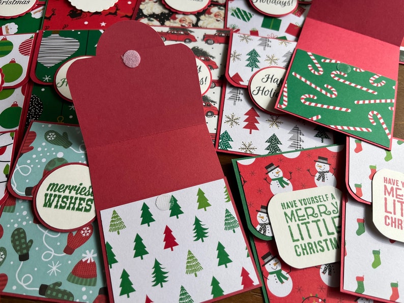 May include: A collection of handmade Christmas cards with various designs, including a red card with a white tree pattern, a green card with candy canes, and a red card with a snowman. The cards have different greetings, including "merriest wishes", "have yourself a merry little Christmas", and "have yourself a merry little Christmas".
