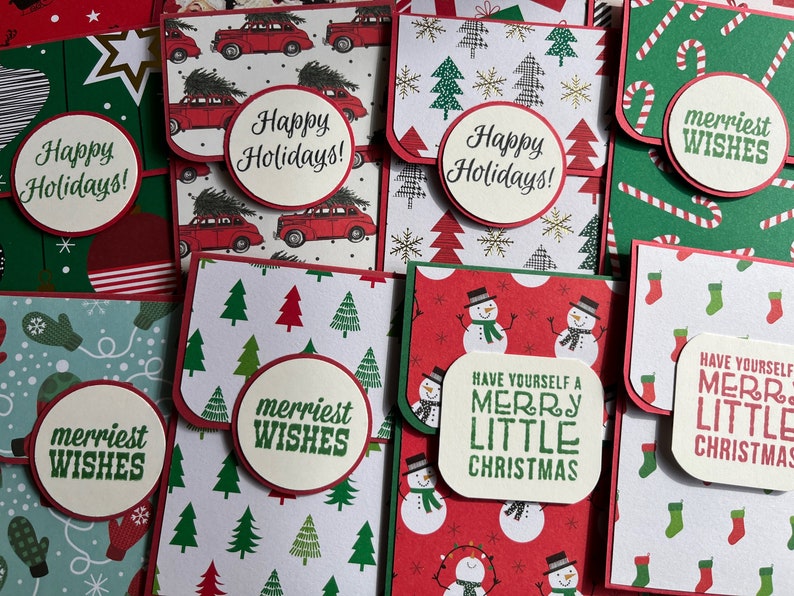 May include: A collection of eight handmade Christmas cards with various holiday themes. The cards feature different designs, including red cars with Christmas trees, snowmen, candy canes, and mittens. The cards have a red and green color scheme and include the phrases "Happy Holidays!" and "Merriest Wishes!"