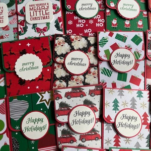 May include: A collection of handmade Christmas card envelopes with various festive designs. The envelopes feature red, green, and white colors with patterns of snowflakes, Christmas trees, Santa Claus, reindeer, and gift boxes. The envelopes have a flap that folds over to create a pocket for cash or a gift card. The text on the envelopes includes "Merry Christmas", "Happy Holidays", and "Have Yourself a Merry Little Christmas".