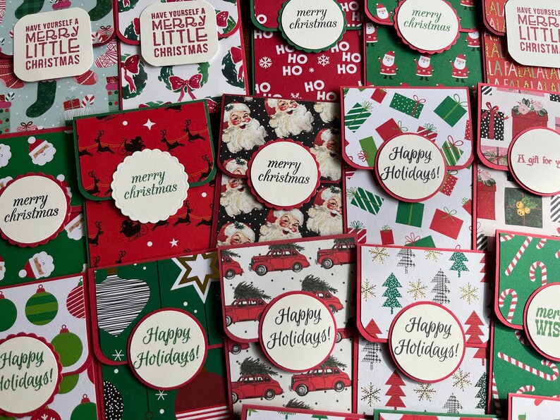 May include: A collection of handmade Christmas card envelopes with various festive designs. The envelopes feature red, green, and white colors with patterns of snowflakes, Christmas trees, Santa Claus, reindeer, and gift boxes. The envelopes have a flap that folds over to create a pocket for cash or a gift card. The text on the envelopes includes "Merry Christmas", "Happy Holidays", and "Have Yourself a Merry Little Christmas".